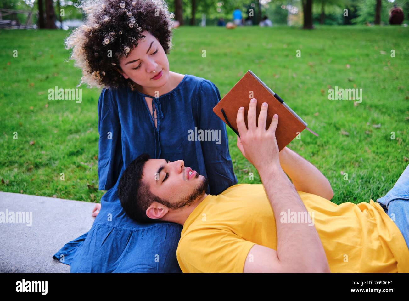 Young man reading book while lying on girlfriend lap at park Stock Photo