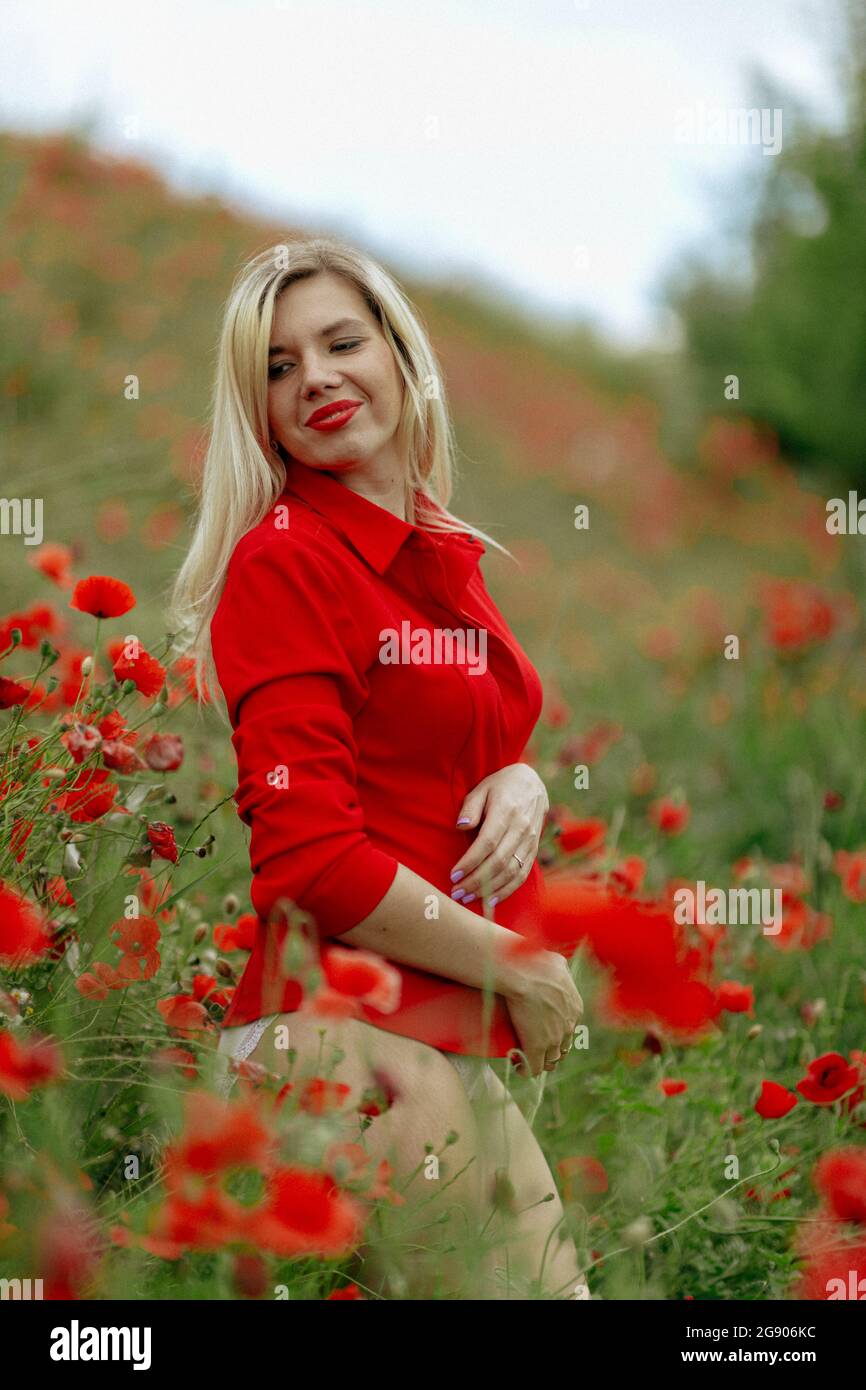 beautiful girl in a field with red poppies in a red shirt Stock Photo