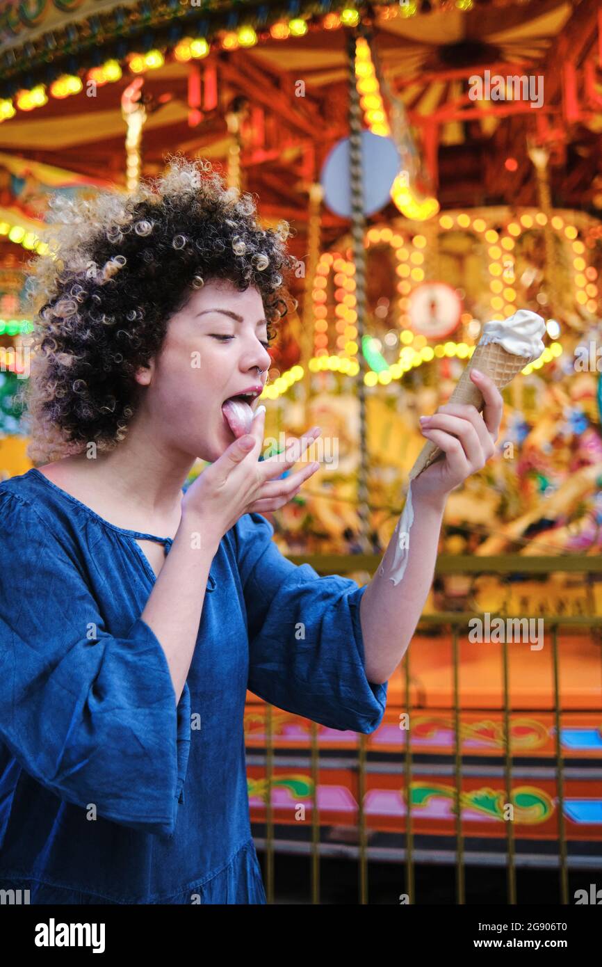 Young woman licking ice cream while standing at amusement park Stock Photo