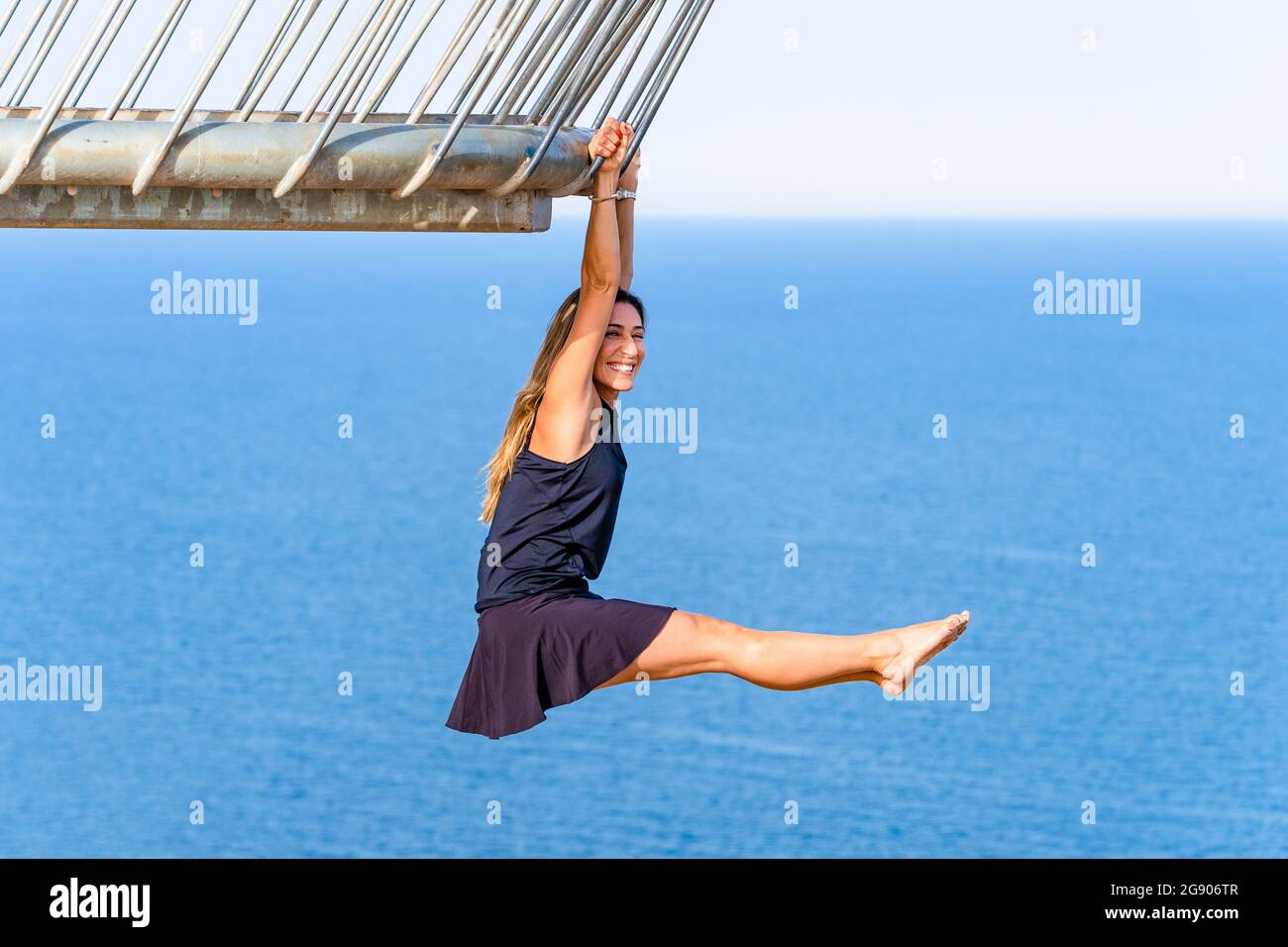 Happy mature woman hanging on railing while practicing acrobatics at viewpoint Stock Photo