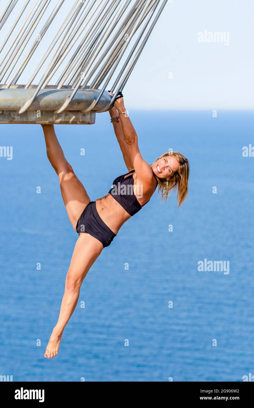 Happy mature woman hanging on railing stretching leg while practicing acrobatics at viewpoint Stock Photo