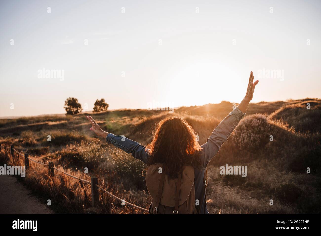Carefree woman standing with arms raised in nature during sunset Stock Photo