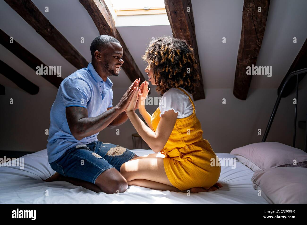 Romantic couple touching hands while sitting on bed in attic at home Stock Photo