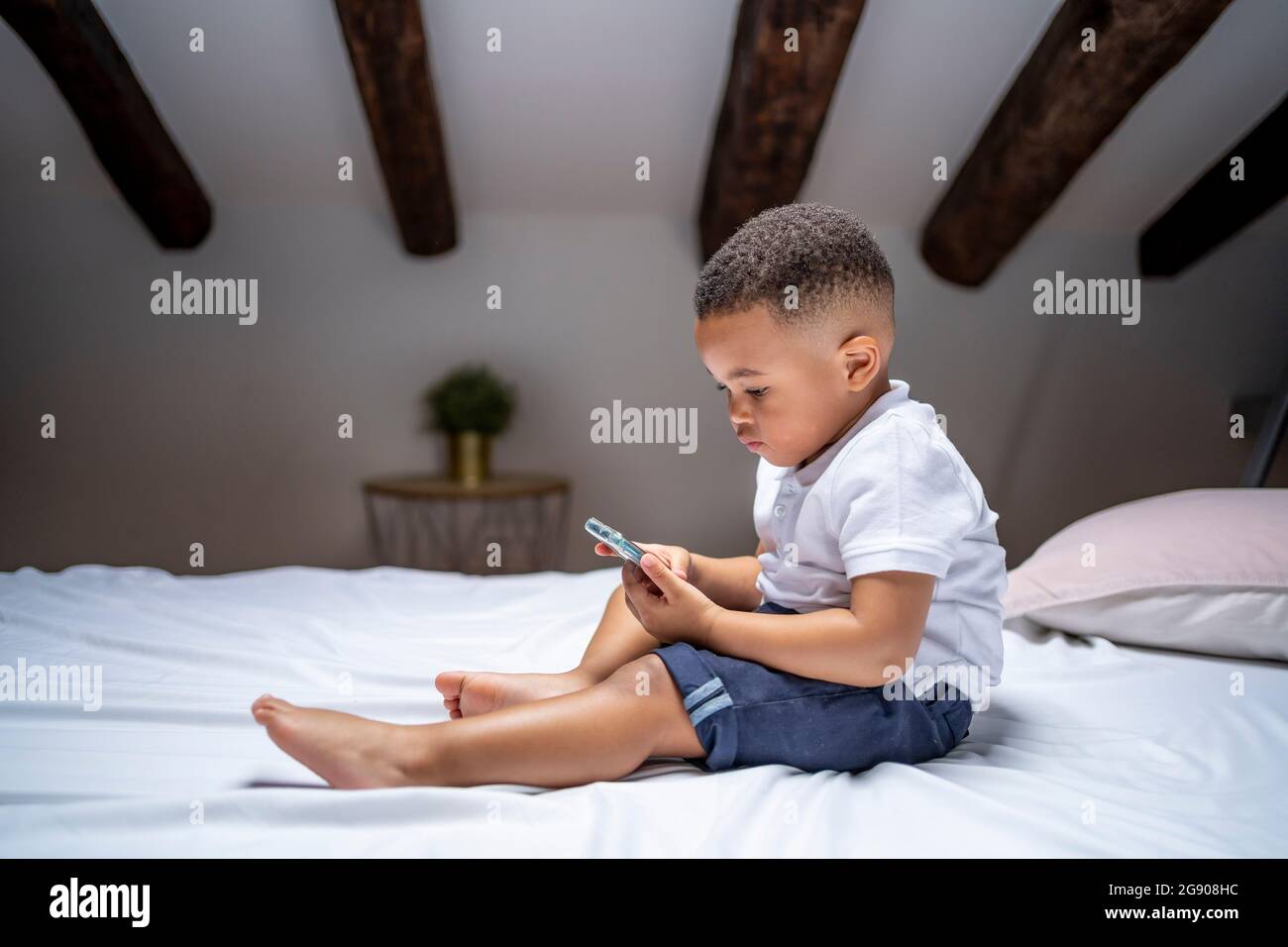 Boy using smart phone while sitting on bed at home Stock Photo