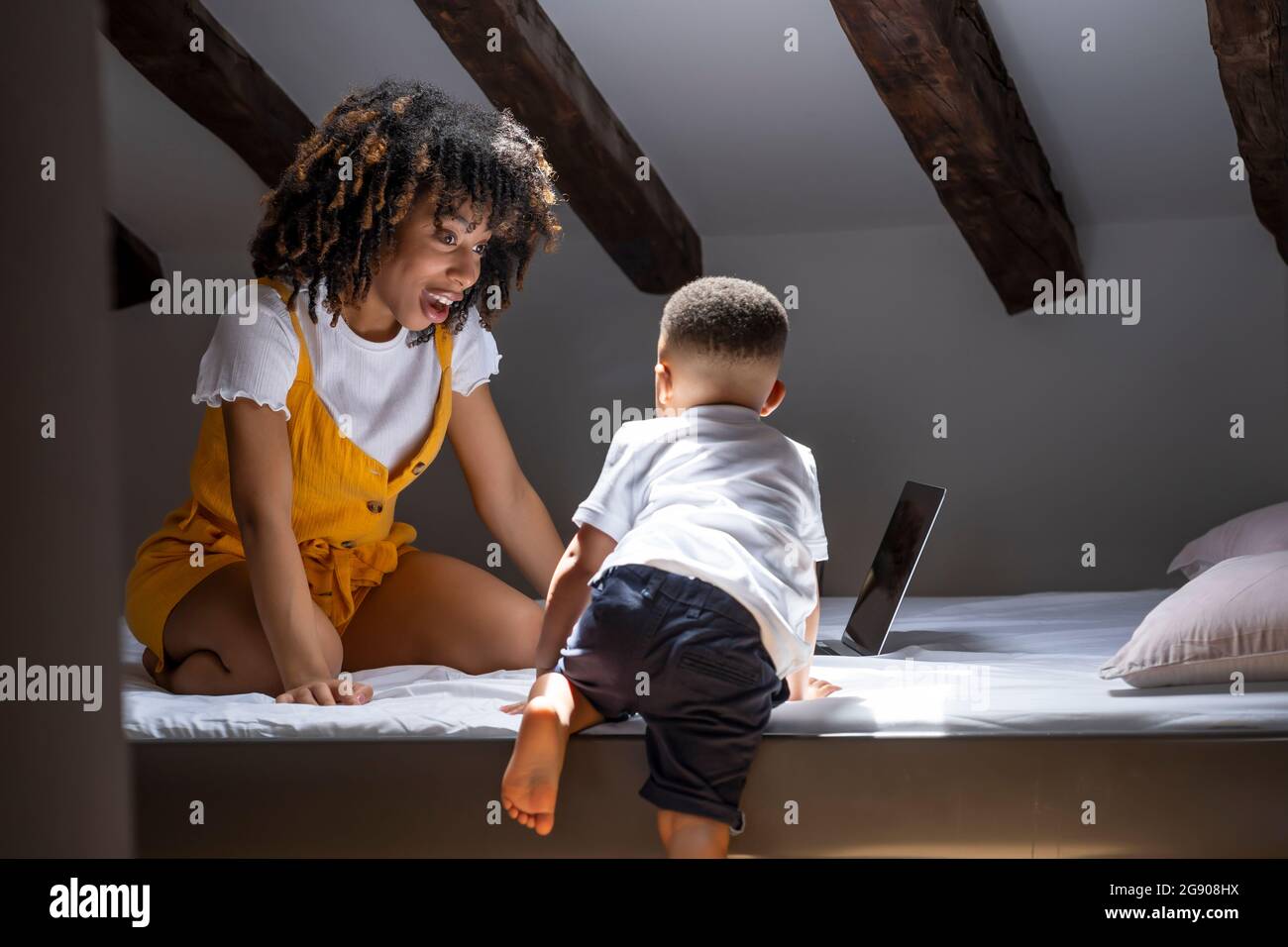 Mother looking at son climbing on bed at home Stock Photo