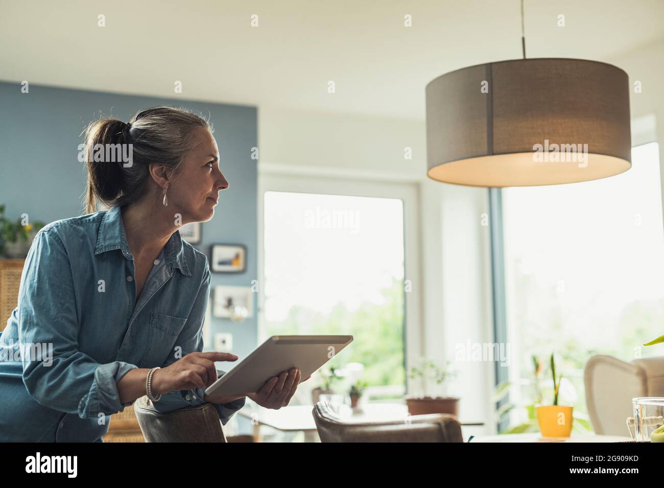 Mature woman turning on lighting equipment with digital tablet at home Stock Photo