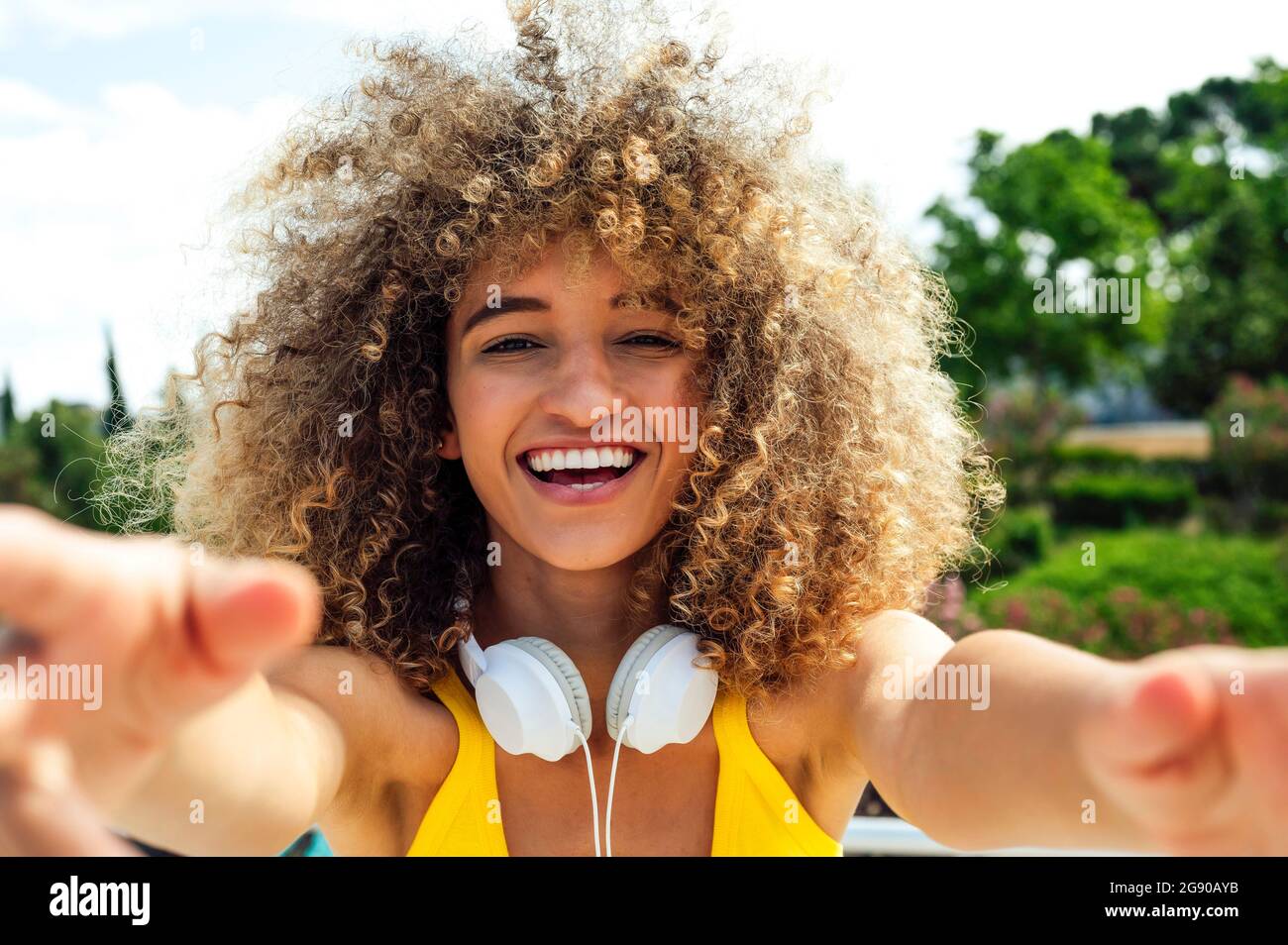 Cheerful curly haired woman wearing headphones on sunny day Stock Photo