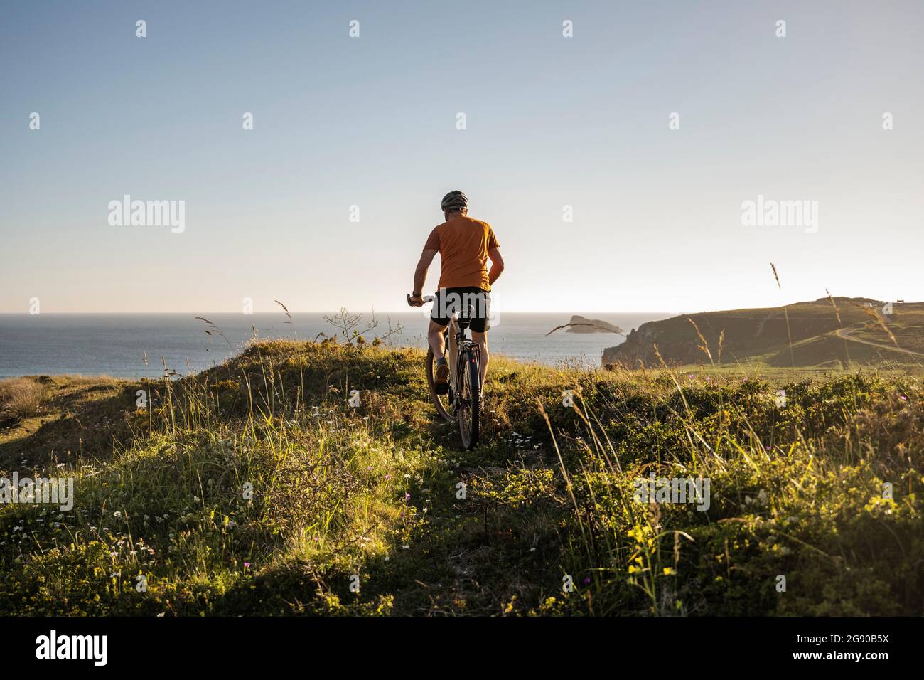 Male sportsperson cycling on green grass at sunset Stock Photo