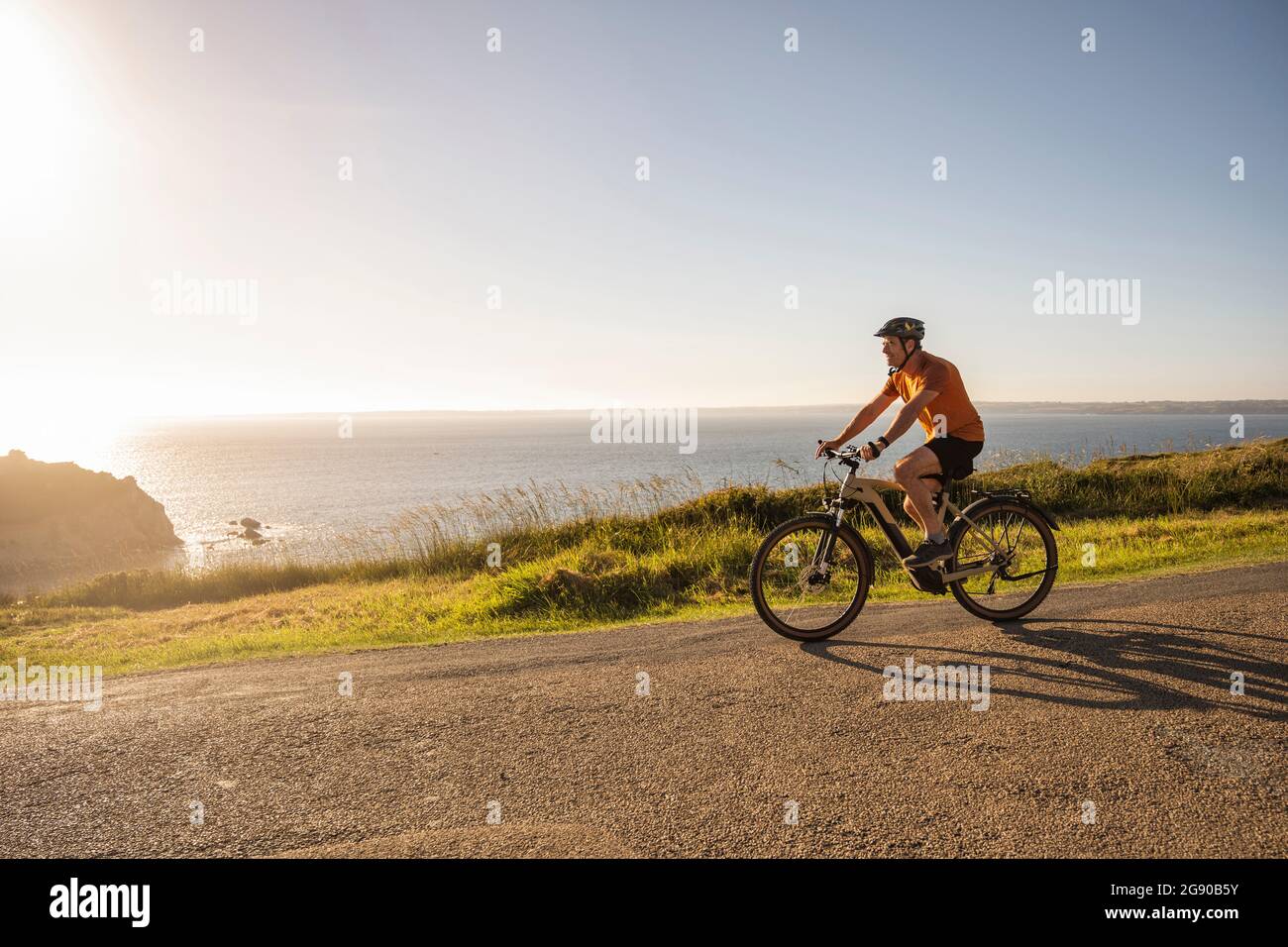Mature sportsman cycling bicycle on road near sea at sunset Stock Photo