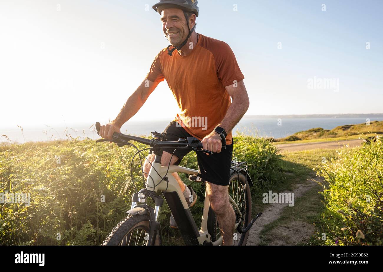 Happy sportsman cycling amidst green plants at sunset Stock Photo