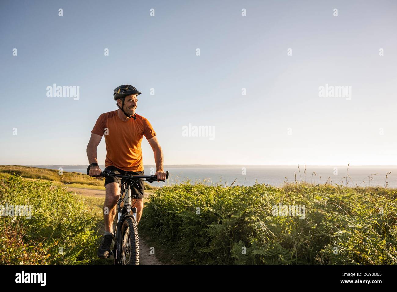 Smiling mature sportsman cycling amidst green grass Stock Photo