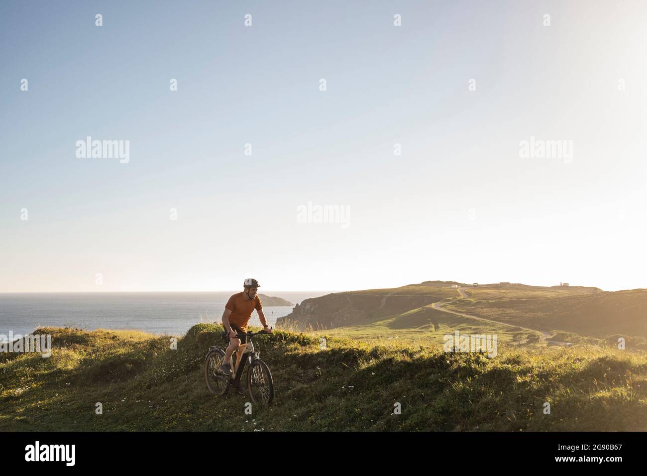 Male athlete cycling on grass near sea at sunset Stock Photo