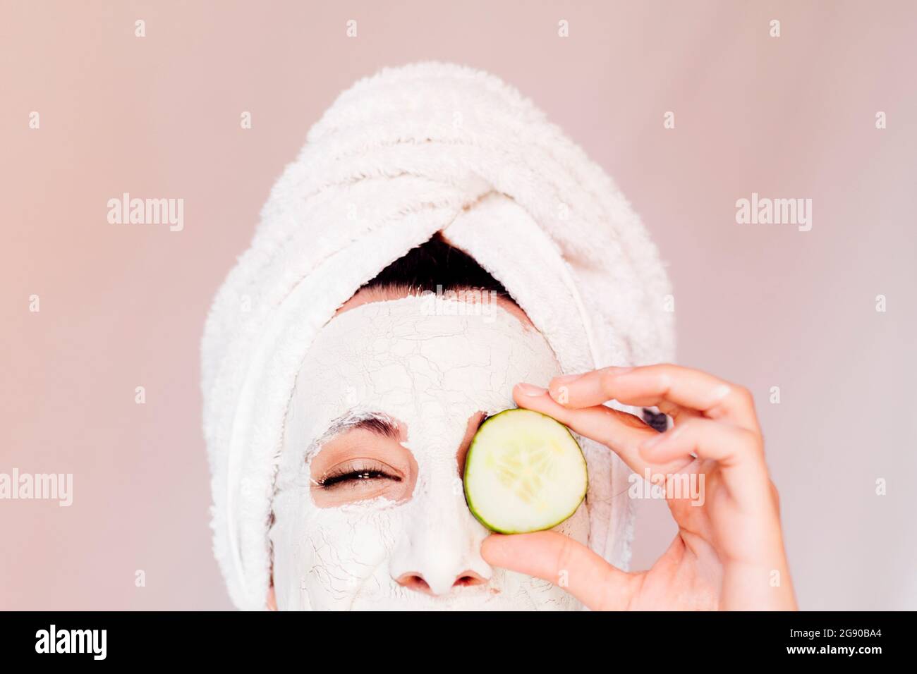 Young woman with beauty face mask covering eye with cucumber slice Stock Photo