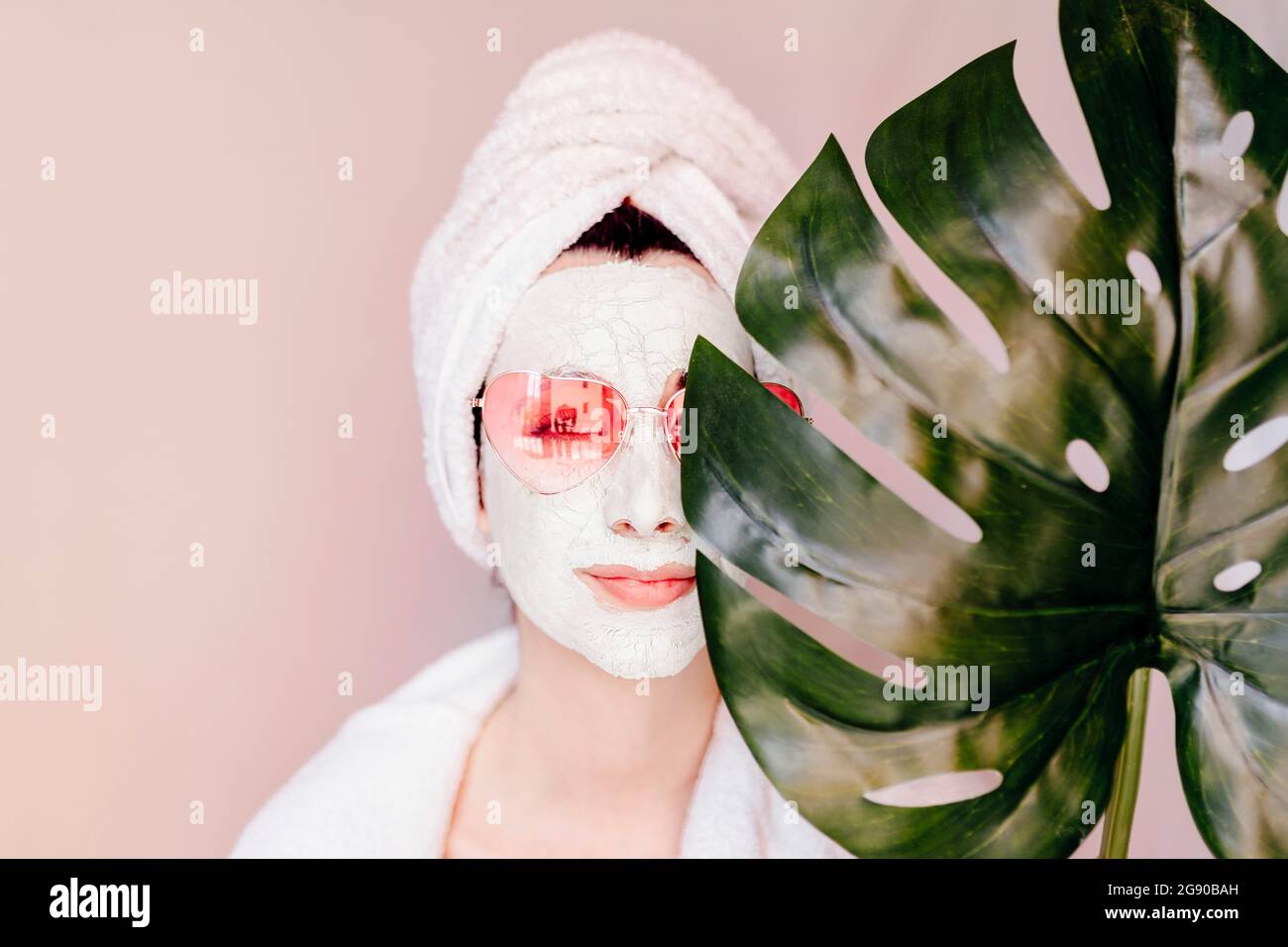 Young woman with beauty face mask covering eye with monstera leaf Stock Photo