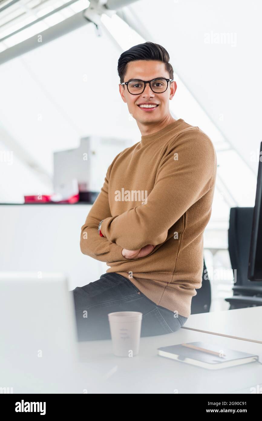 Confident businessman with arms crossed sitting on desk Stock Photo - Alamy