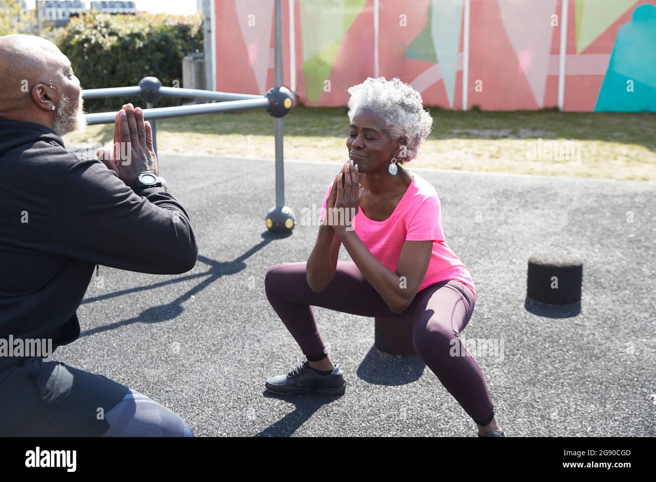 Senior woman with hands clasped exercising in front of man at park Stock Photo