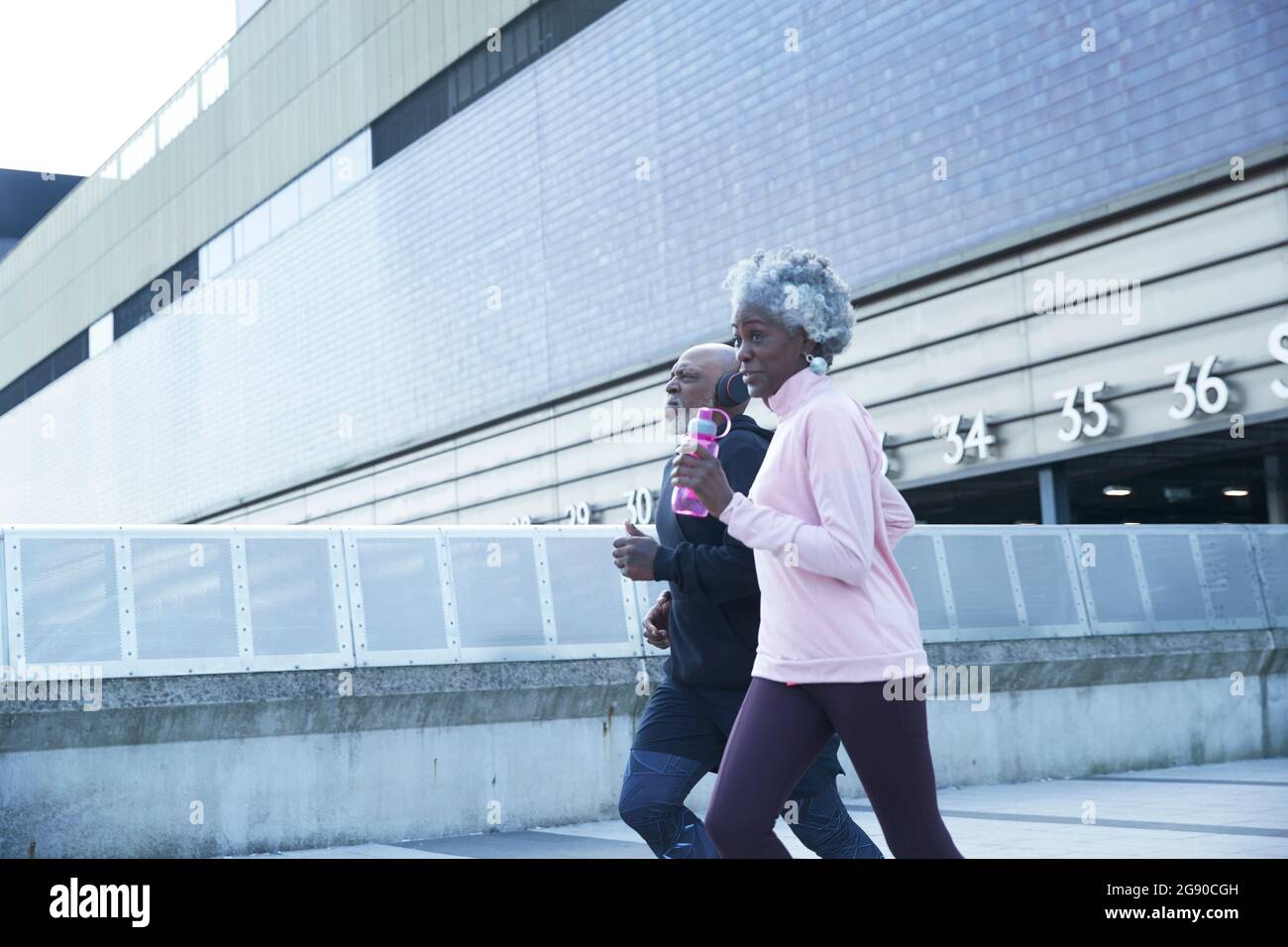 Senior woman holding water bottle while running with man in city Stock Photo