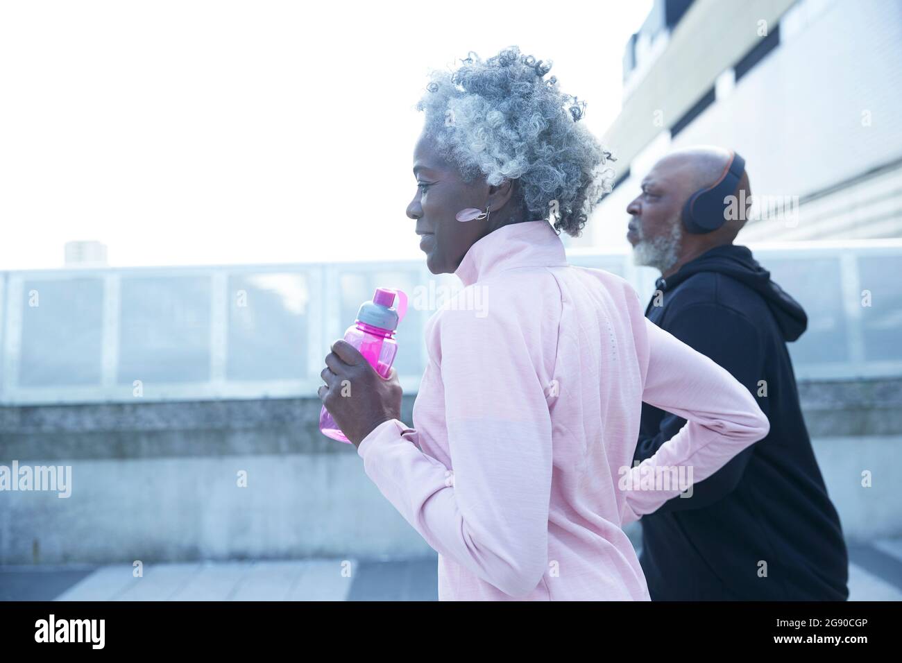 Senior woman holding water bottle while running with mature man Stock Photo