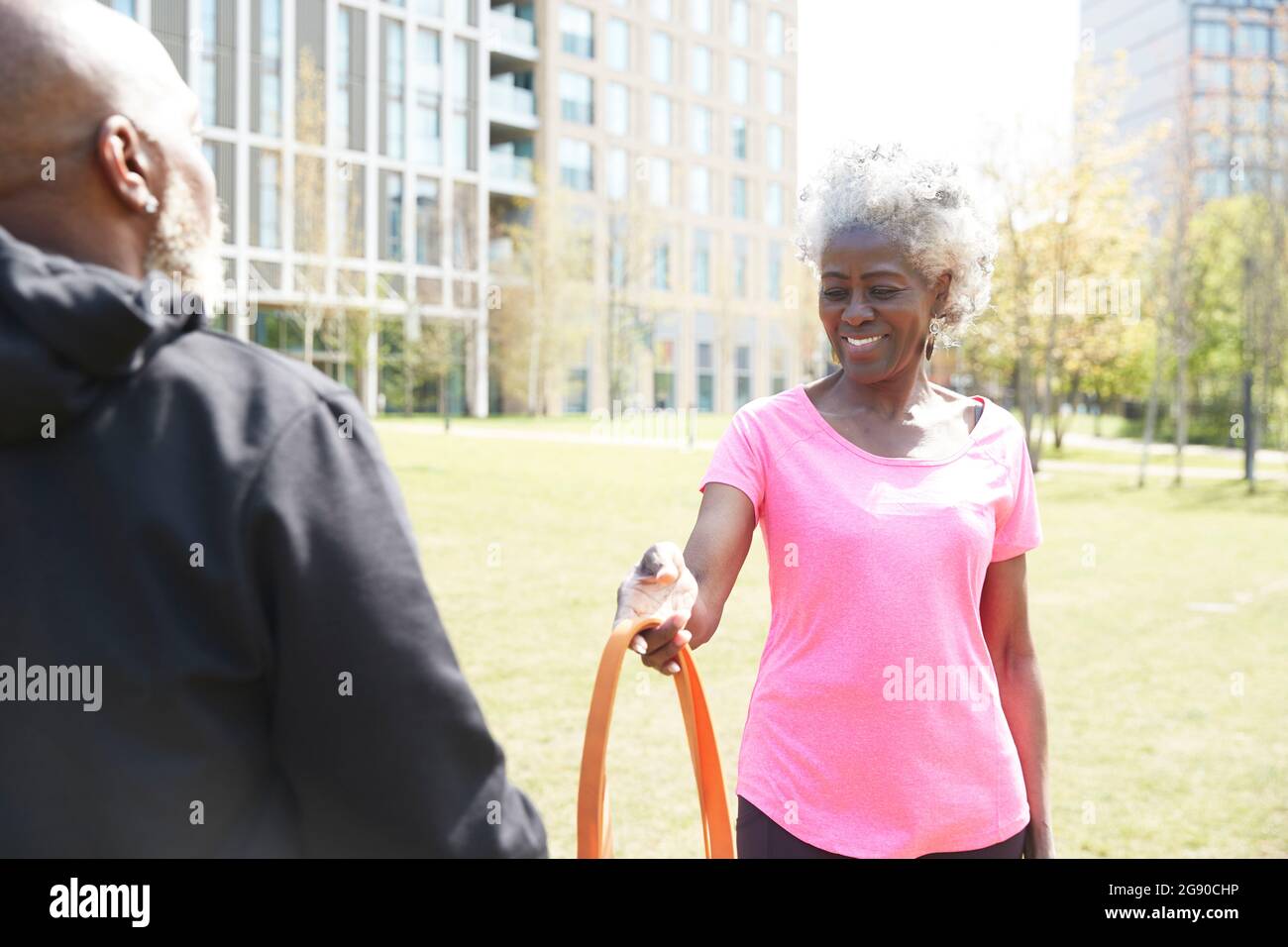 Smiling woman giving resistance band to man at park Stock Photo