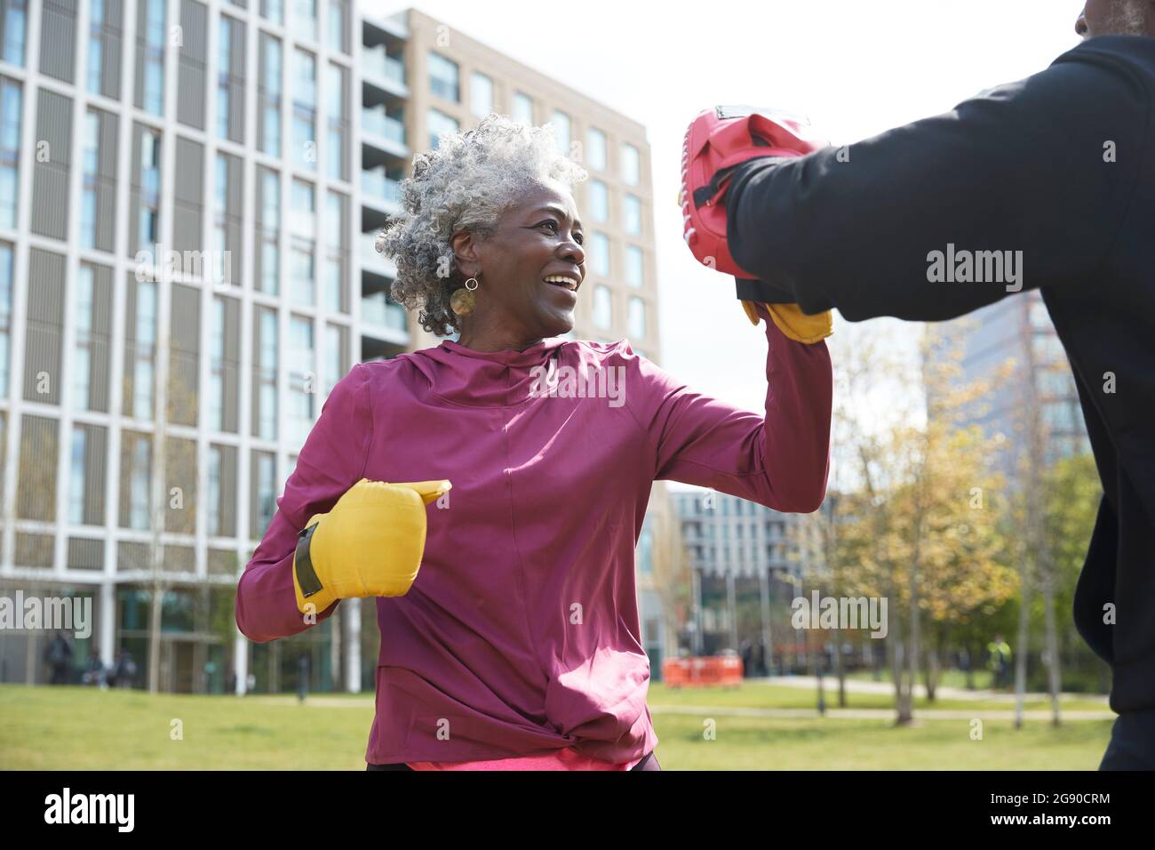 Smiling woman practicing boxing with man at park on sunny day Stock Photo