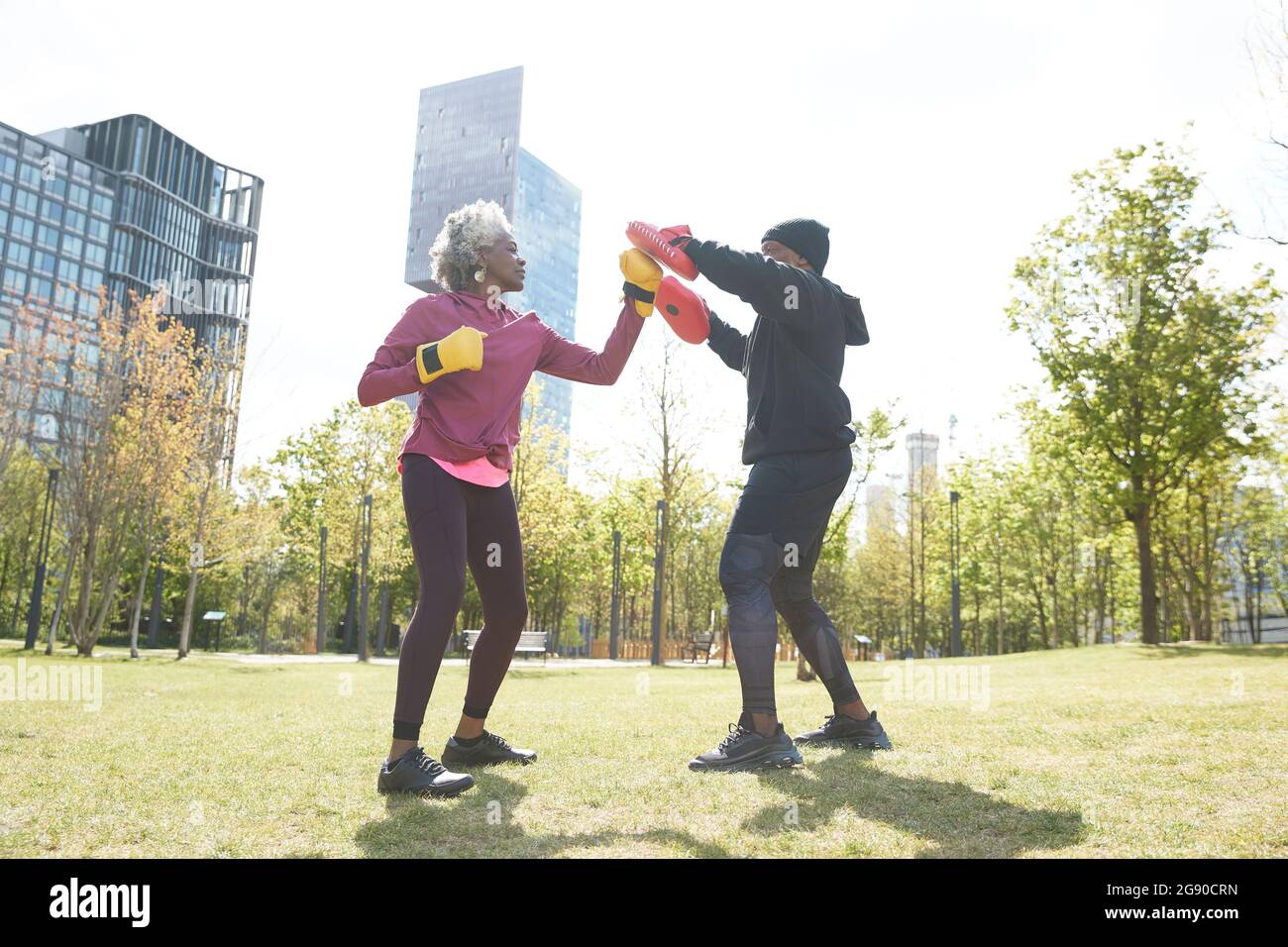 Senior woman practicing boxing with man at park on sunny day Stock Photo