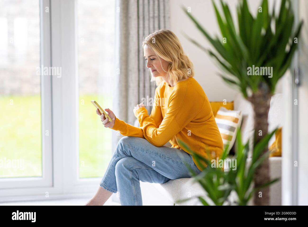 Woman sitting with legs crossed at knee using smart phone on sofa at home Stock Photo