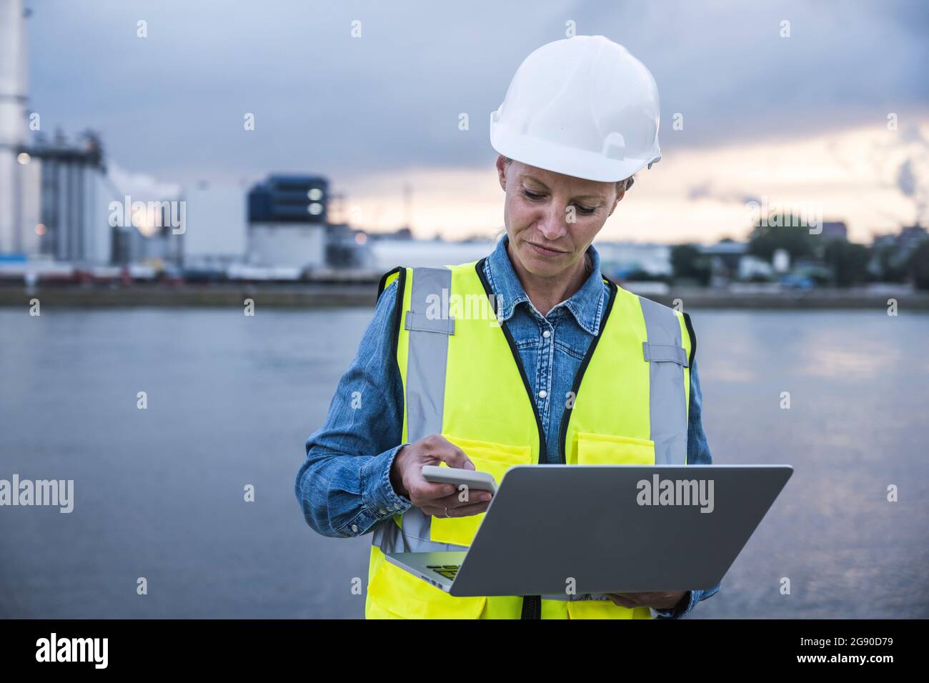 Female professional using smart phone while holding laptop Stock Photo ...