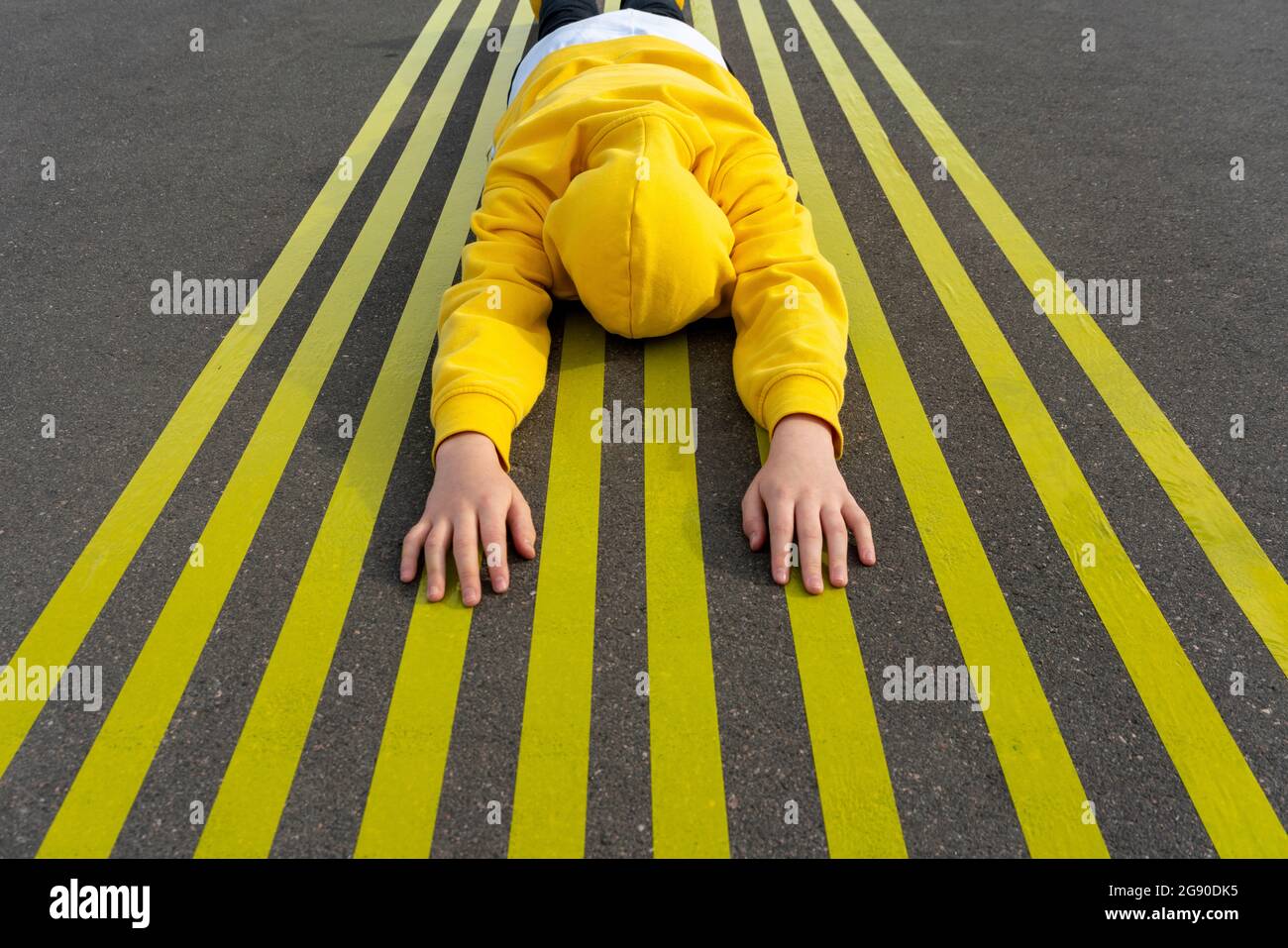 Boy with arms raised lying over yellow markings on road Stock Photo Alamy