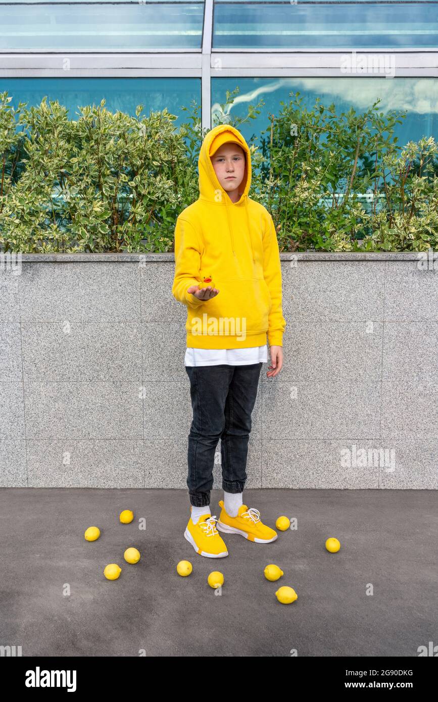 Boy holding rubber duck while standing amidst lemons Stock Photo