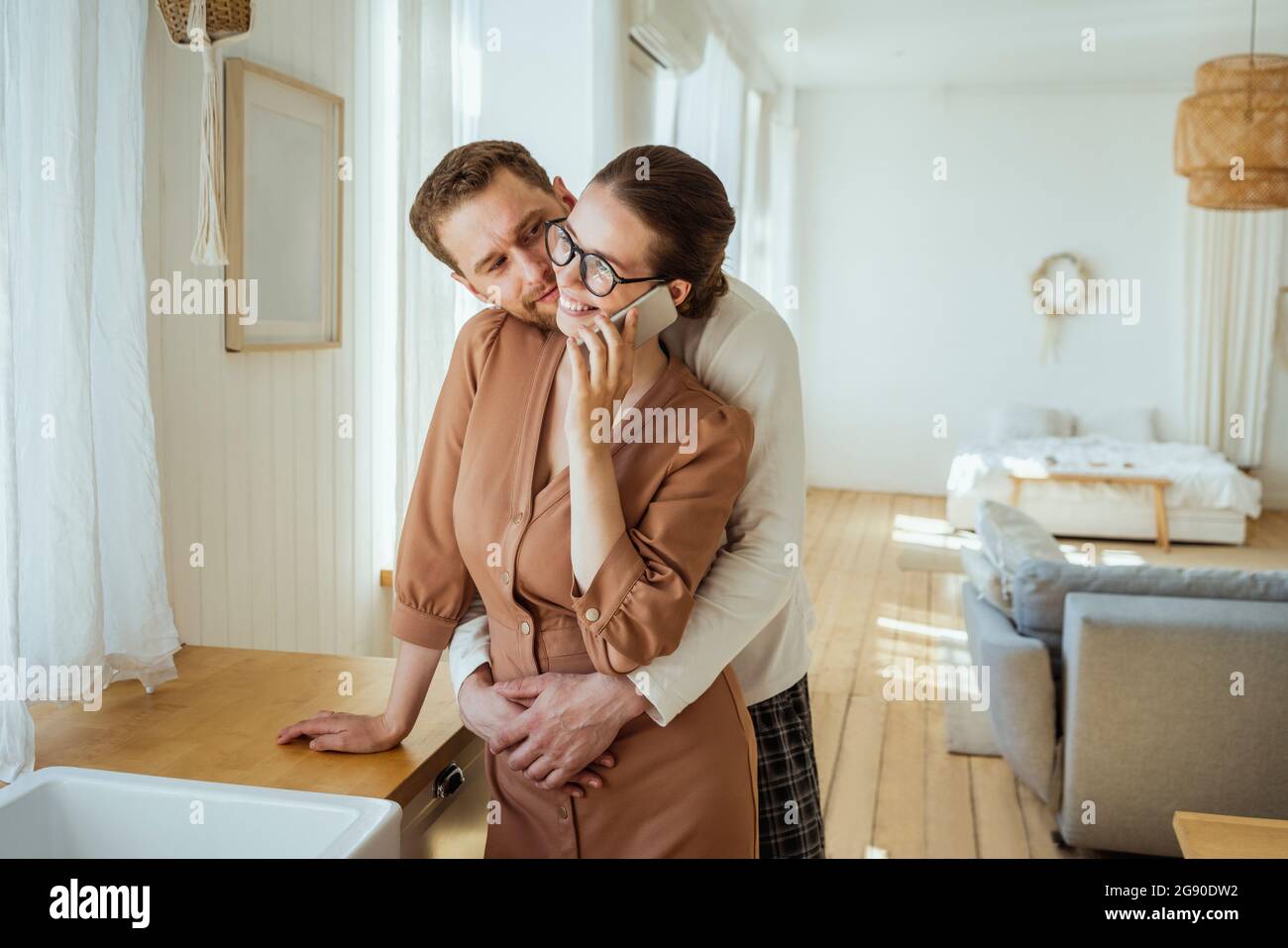 Man embracing woman talking on mobile phone at home Stock Photo