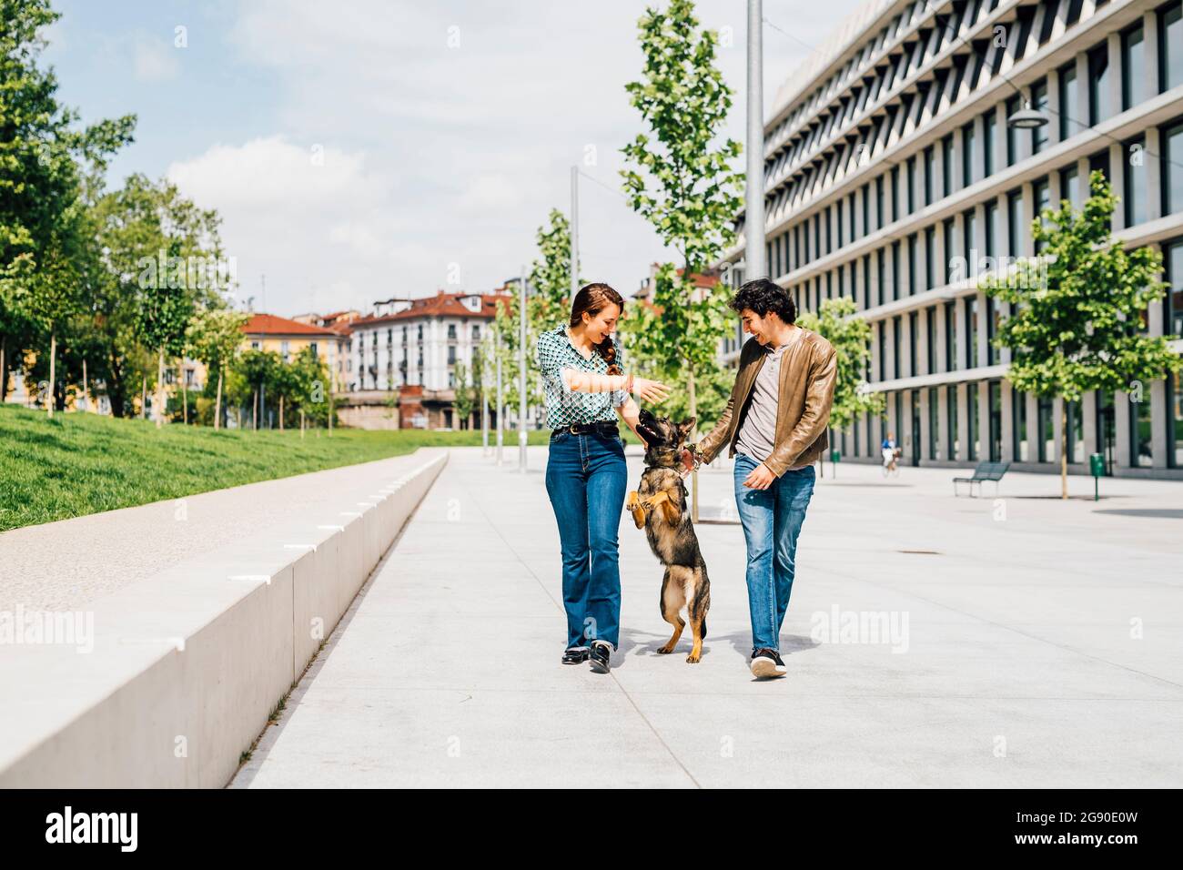 Couple playing with dog while walking on city street Stock Photo