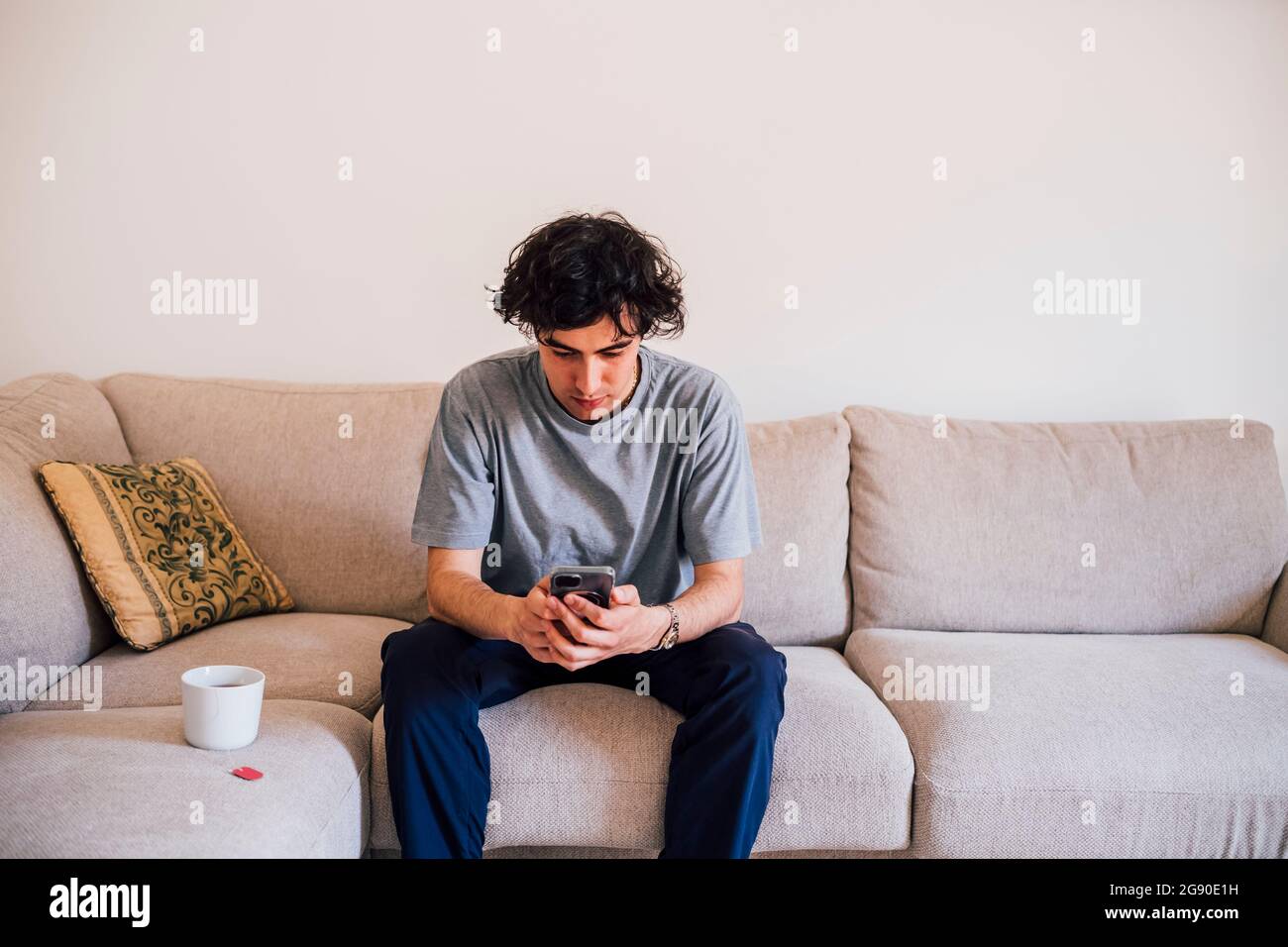 Man using mobile phone while sitting by coffee cup on sofa Stock Photo