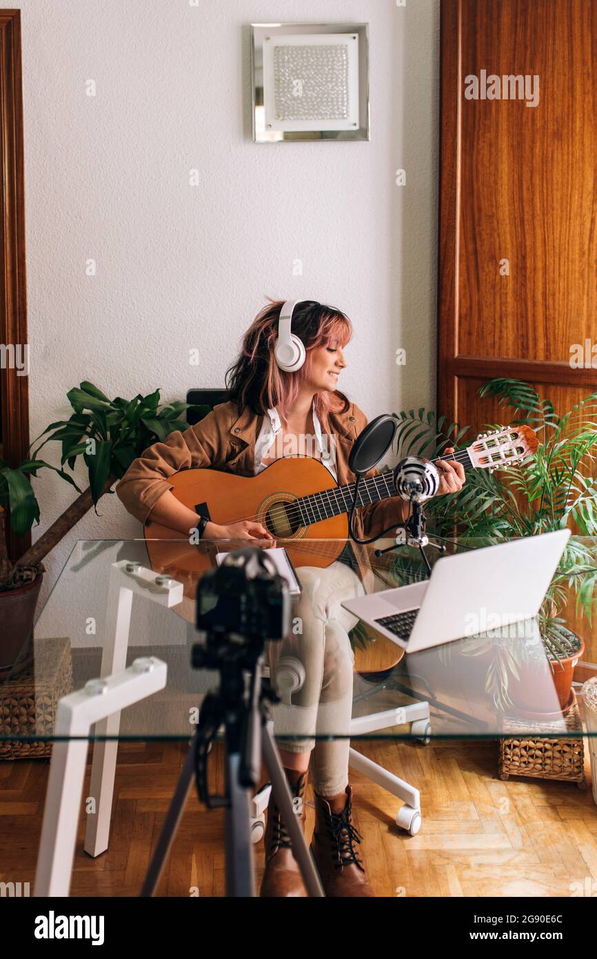 Woman playing guitar while filming at home Stock Photo