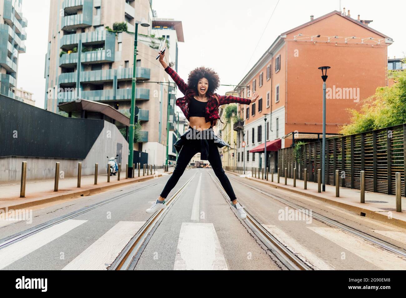 Carefree woman jumping with arms outstretched on railroad tracks Stock