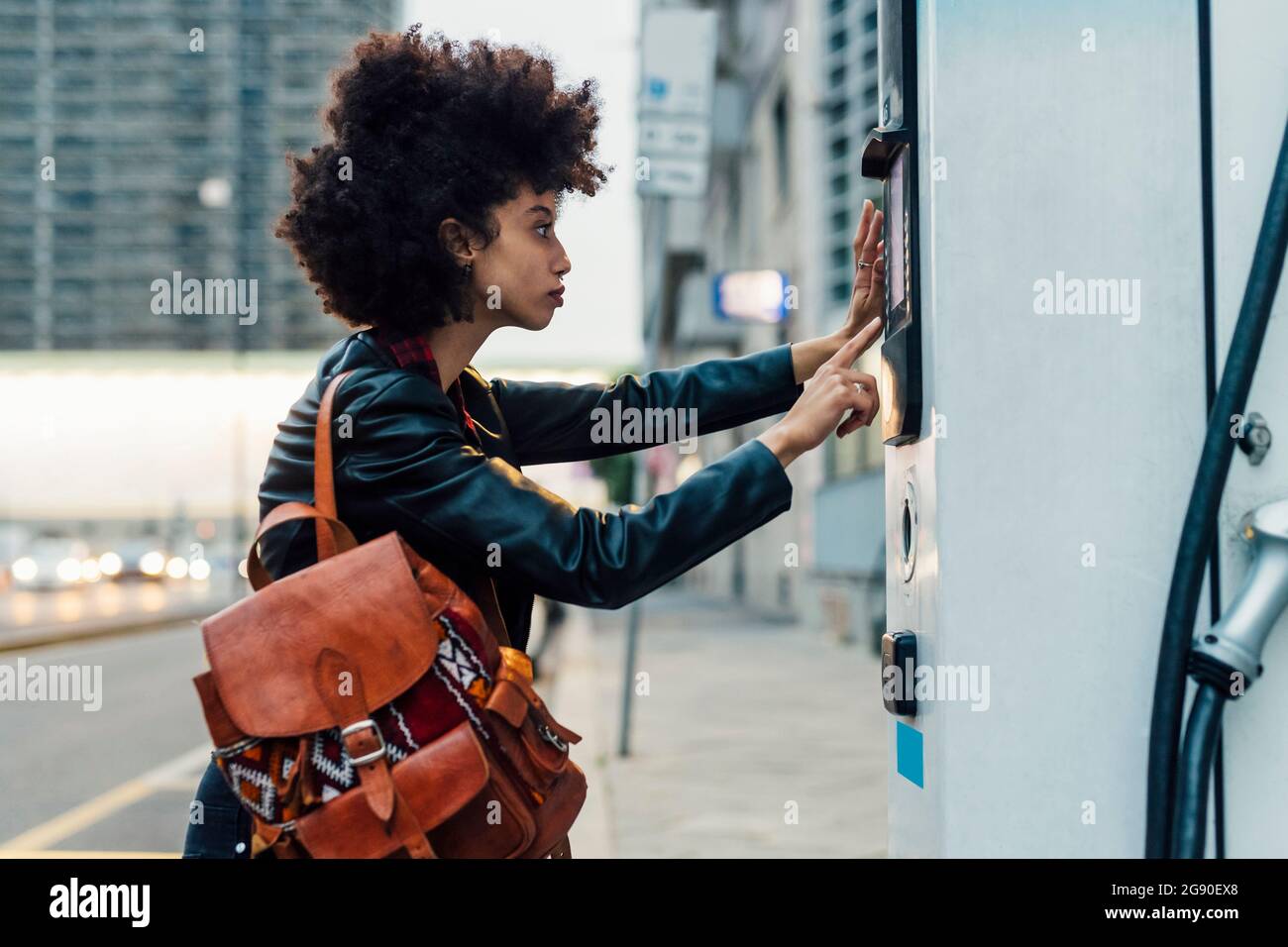 Woman with backpack using ticket machine at electric vehicle charging ...