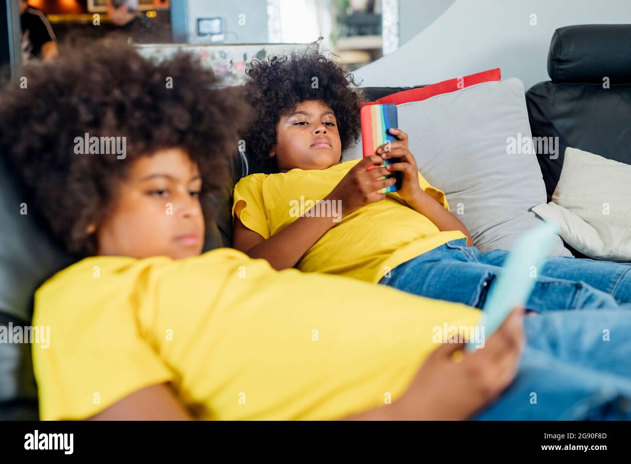 Twin brothers using wireless technologies on sofa at home Stock Photo