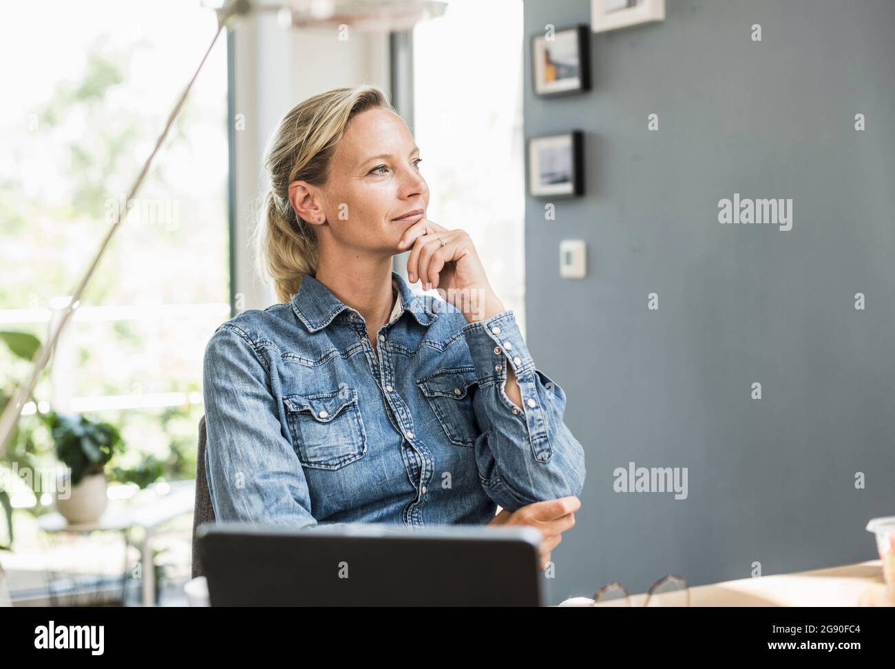 Thoughtful businesswoman with hand on chin sitting at home Stock Photo ...