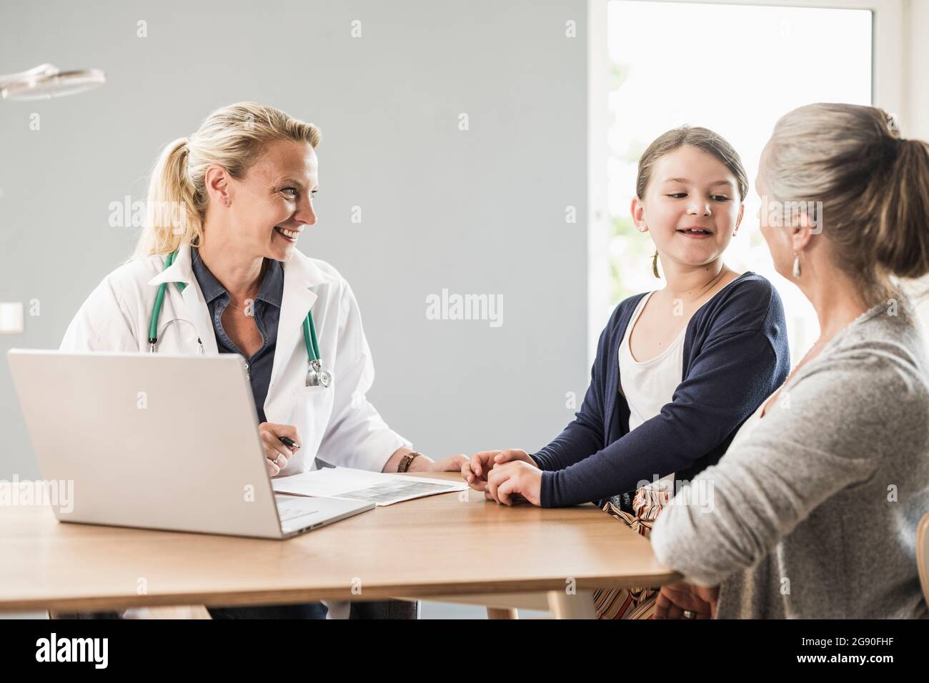Daughter talking with mother while sitting by doctor at office Stock Photo