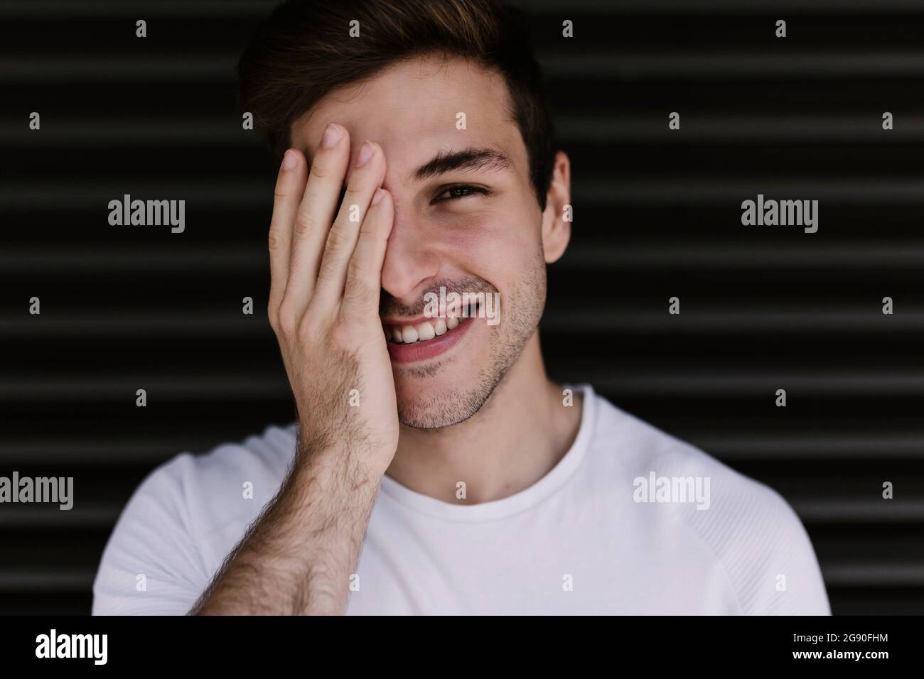 Smiling man covering eye with hand Stock Photo - Alamy
