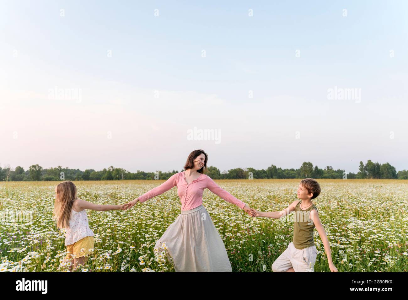 Mother holding hands of children while walking amidst flowers in field Stock Photo