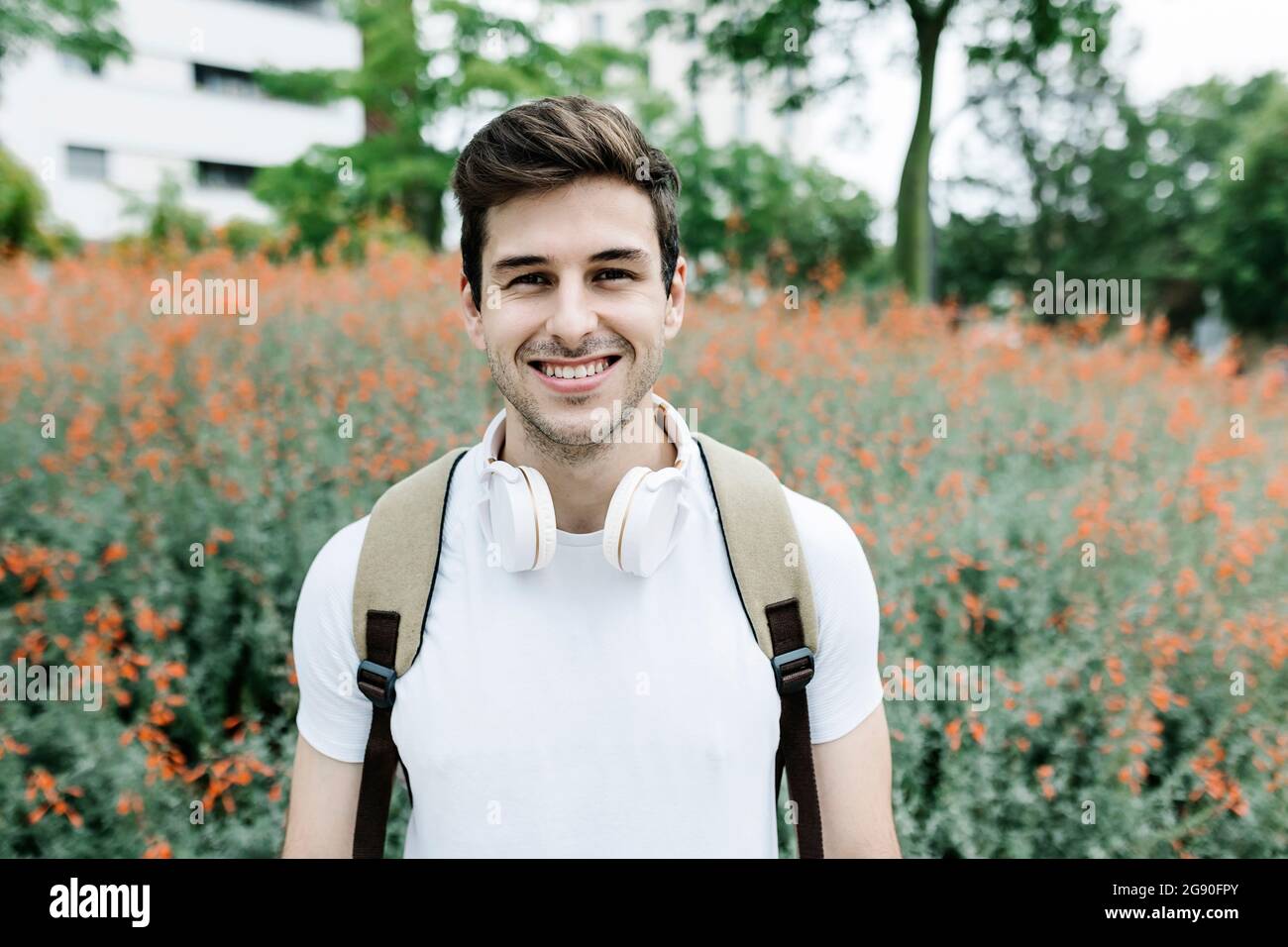 Smiling young man carrying backpack while standing in front of meadow Stock Photo