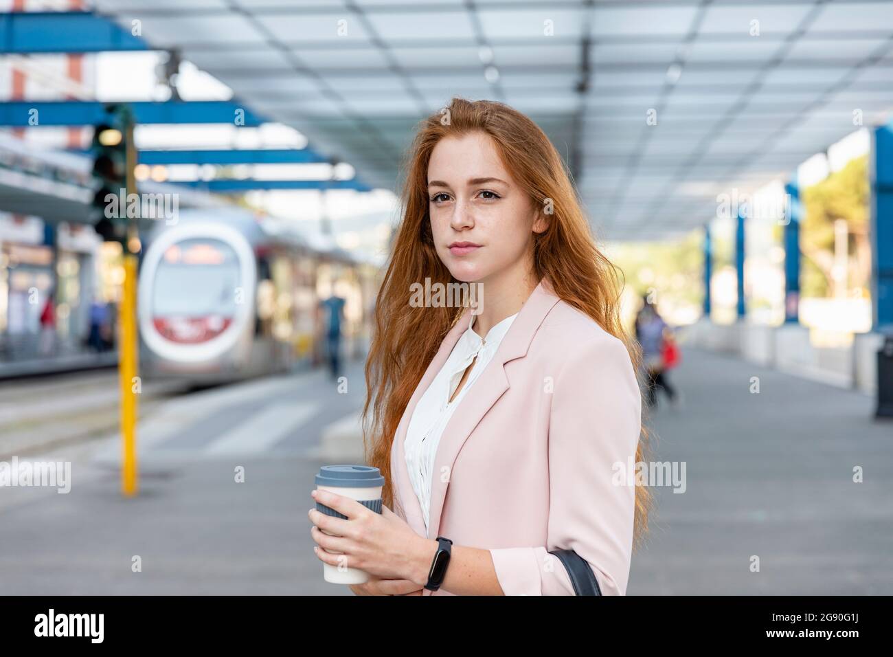 Beautiful female freelancer looking away while holding disposable coffee cup on railway platform Stock Photo
