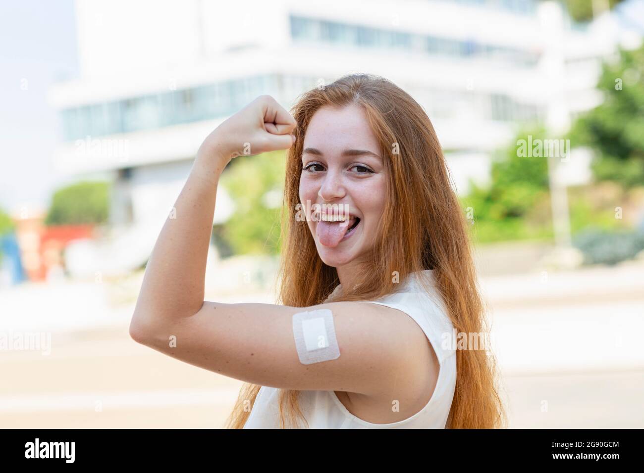 Businesswoman with bandage on arm sticking out tongue during pandemic Stock Photo