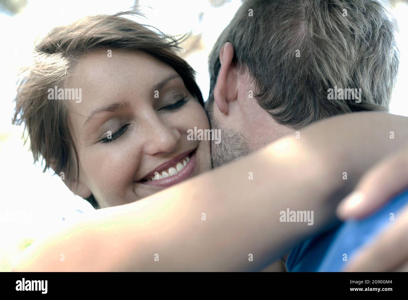 Smiling young woman with eyes closed embracing man at park Stock Photo