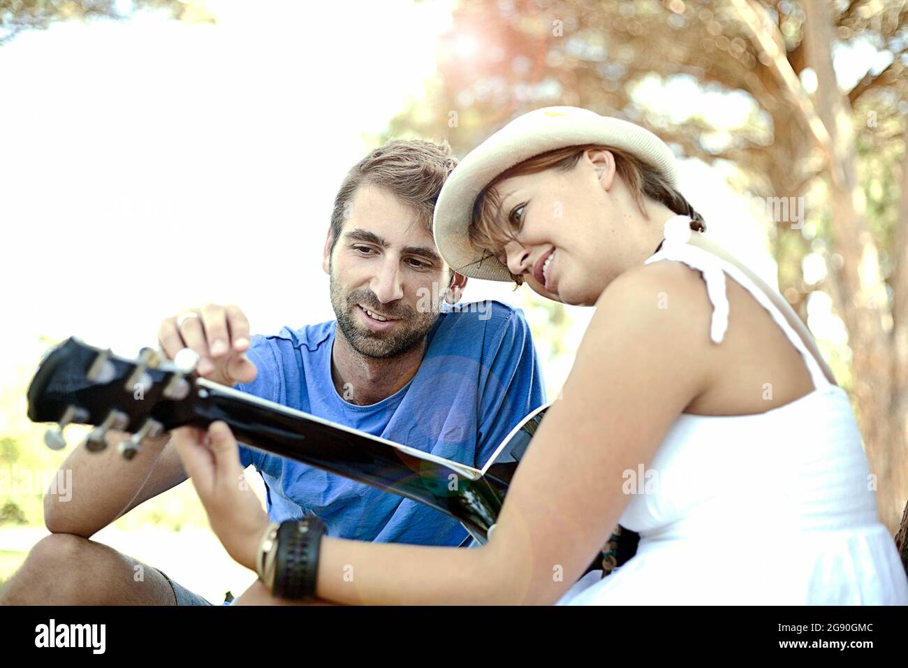 Young man teaching guitar to girlfriend at park Stock Photo