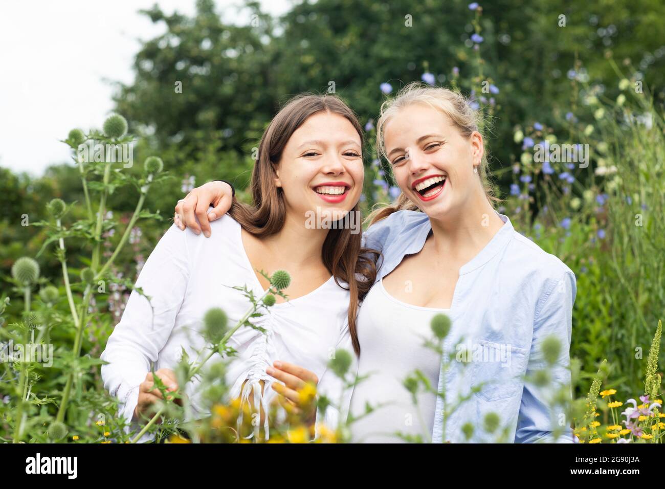 Happy female friends amidst flowering plant in nature Stock Photo