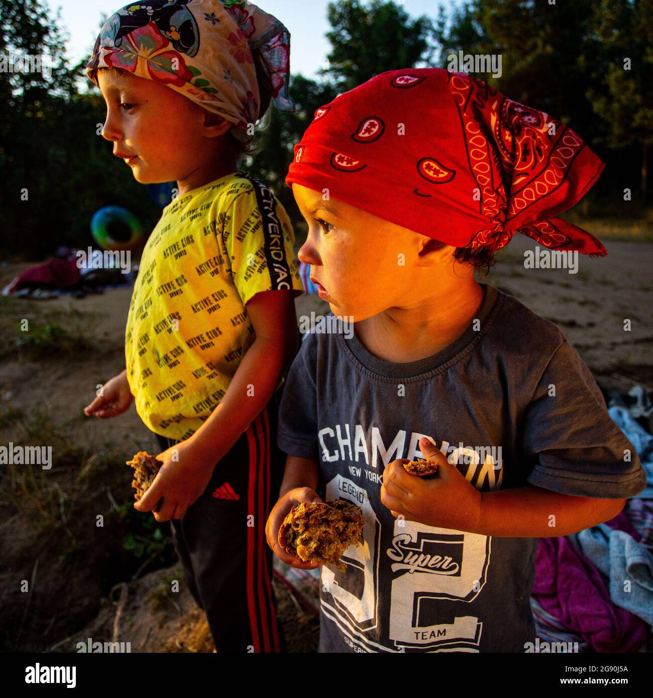Two eating kids (brother and sister) enjoy summer time on the shore of a lake in Kiev, Ukraine, keep holding in hands pieces of bread to feed ducks. Stock Photo