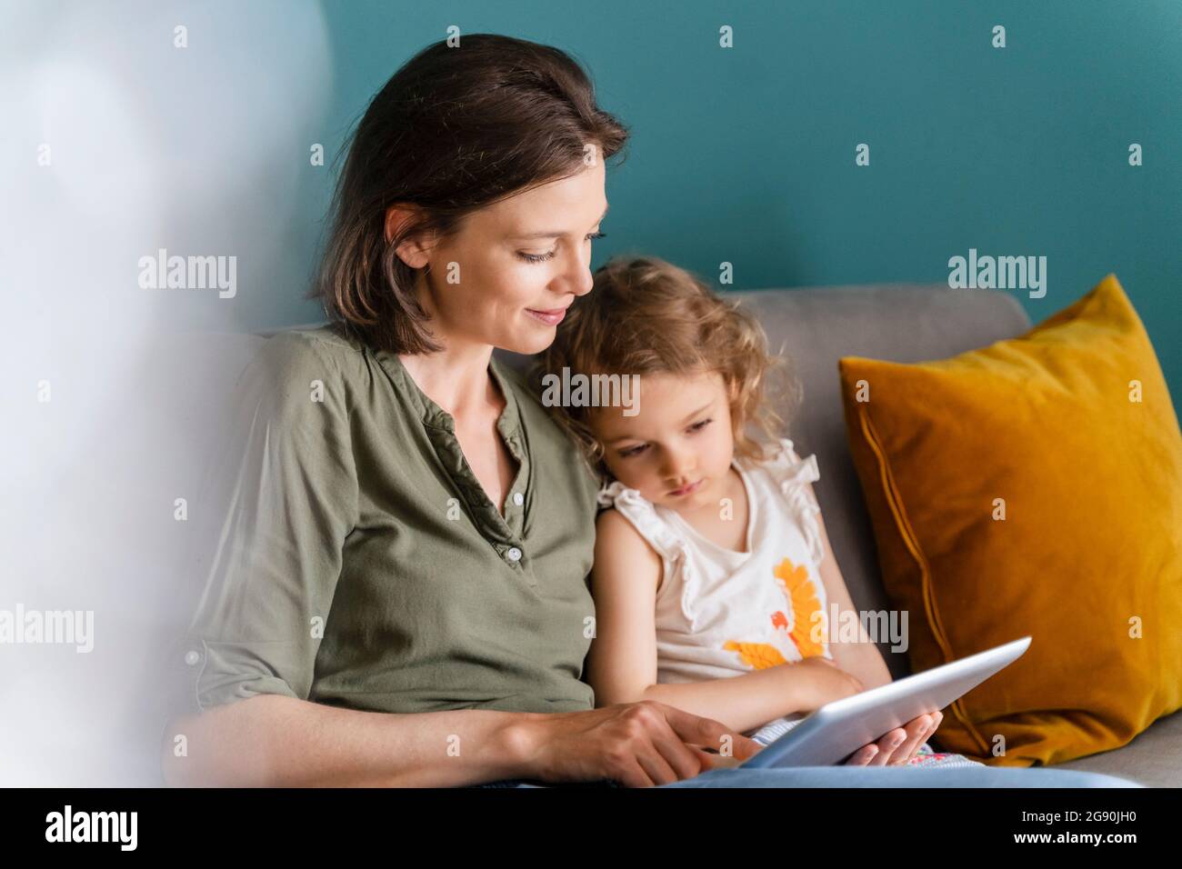 Mother using digital tablet while sitting with daughter at home Stock Photo