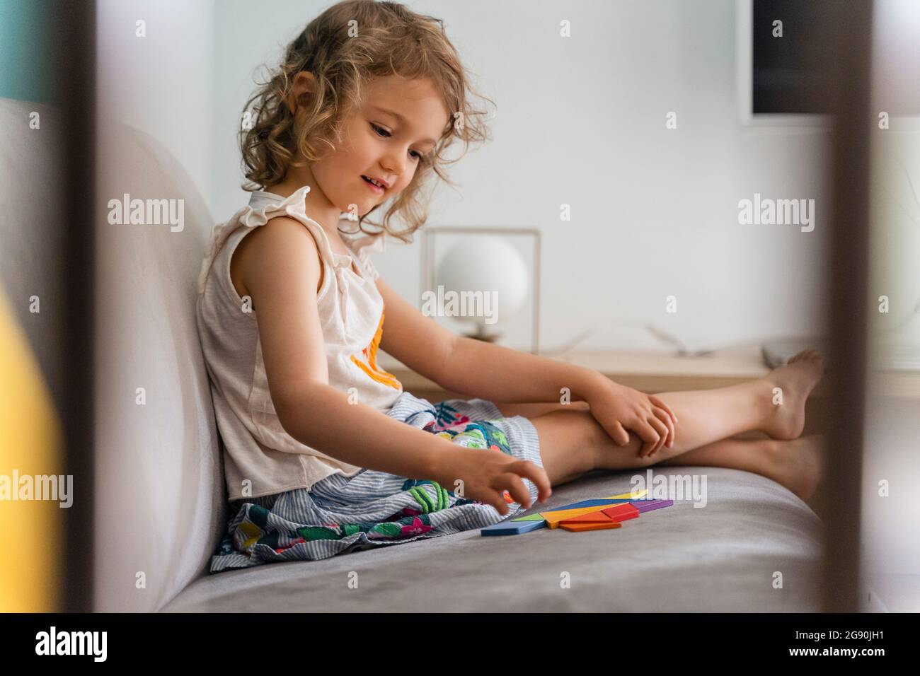 Smiling girl arranging puzzle while sitting at home Stock Photo