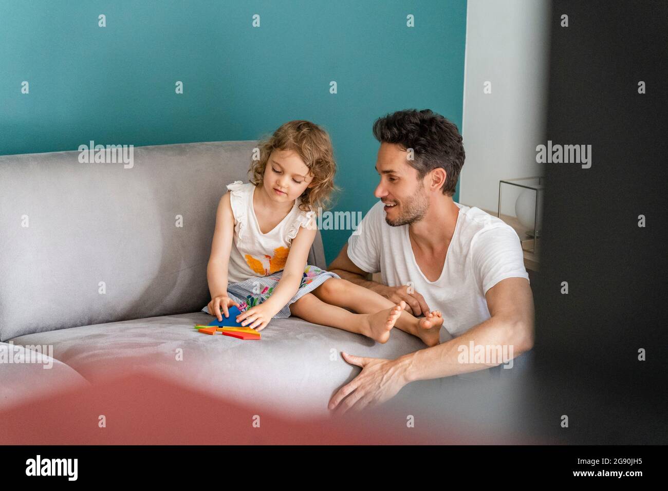 Daughter playing with puzzle while sitting by father in living room Stock Photo